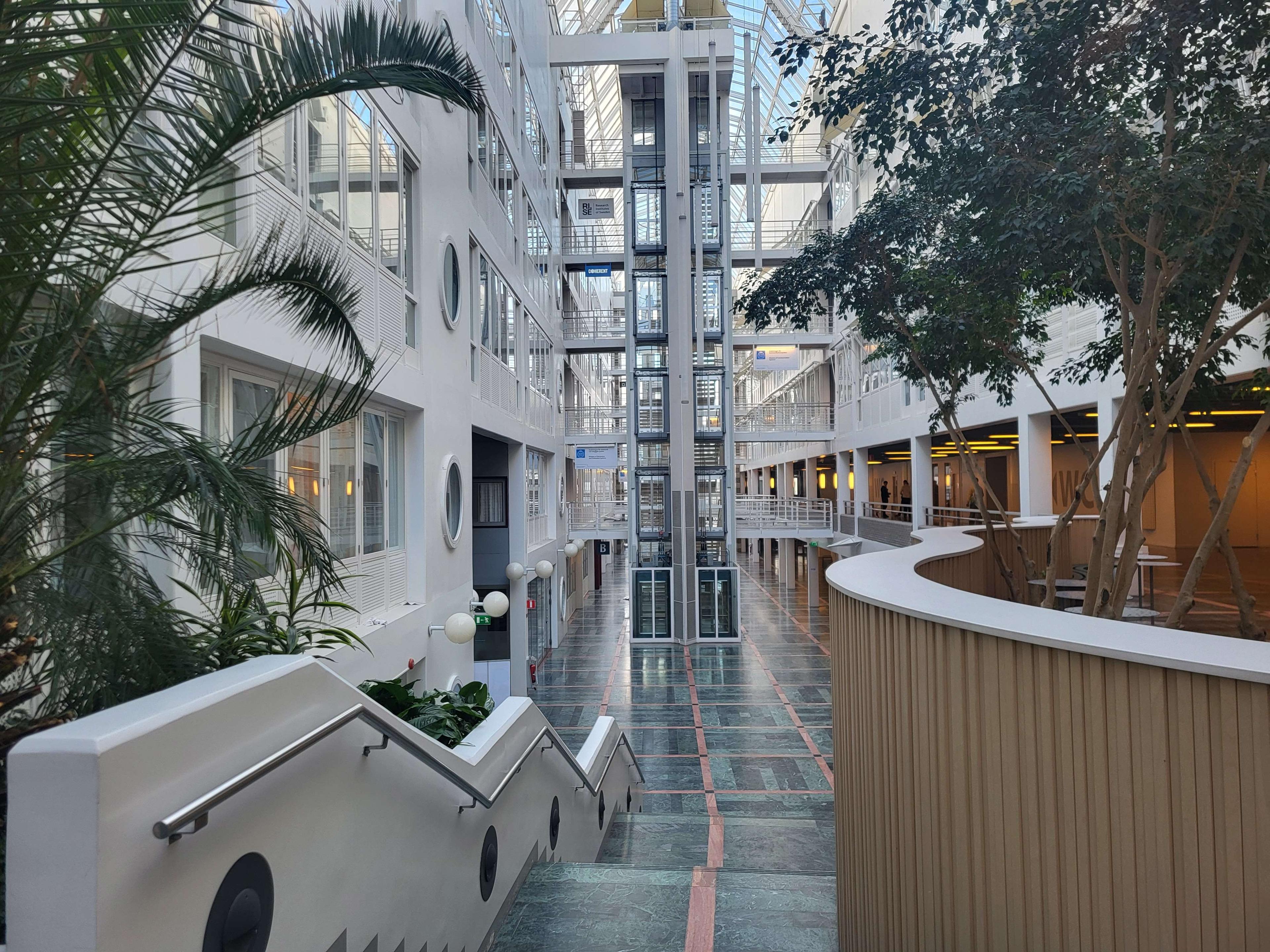 Inuti Electrum på andra våningen med utsikt mot hissarna i mitten och träd på båda sidor om trappan ner.