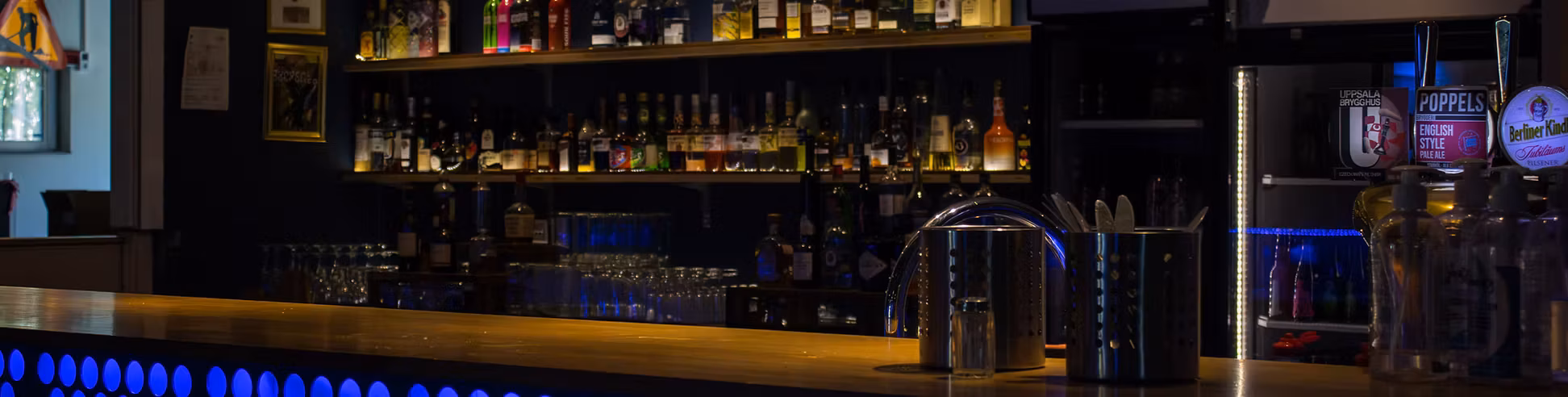 The bar in Kistan 2.0 with loads of bottles and refrigerators in the background.